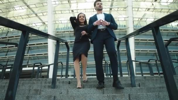 Два бизнес-партнера спускаются по лестнице рядом с современным зданием — стоковое видео