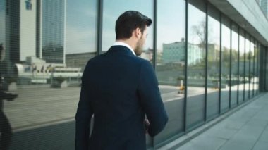 Back view businessman walking with phone. Man using smartphone outdoors