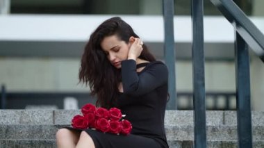 Closeup woman sitting with roses at street. Woman throwing roses on stairs