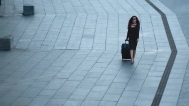 Sokakta elinde bavulla dolaşan bir kadın. Dışarıda güneş gözlüğü takan kadın.