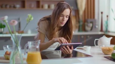 Attractive woman using digital tablet on kitchen. Girl browsing internet on pad