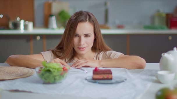 Привлекательная женщина выбирает между салатом и тортом на столе. Концепция здорового питания — стоковое видео