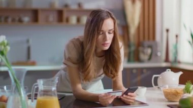 Woman taking on smartphone at kitchen. Lady drinking coffee in morning at home