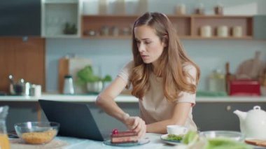 Businesswoman working on laptop at home office. Girl eating cake on kitchen