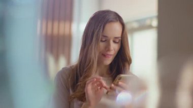 Woman typing on smartphone on kitchen. Lady texting message on mobile phone
