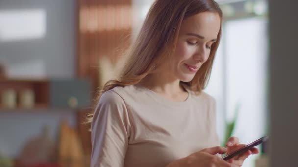 Mensaje de texto de la mujer en el teléfono inteligente en la cocina. Señora usando el teléfono celular en casa — Vídeos de Stock