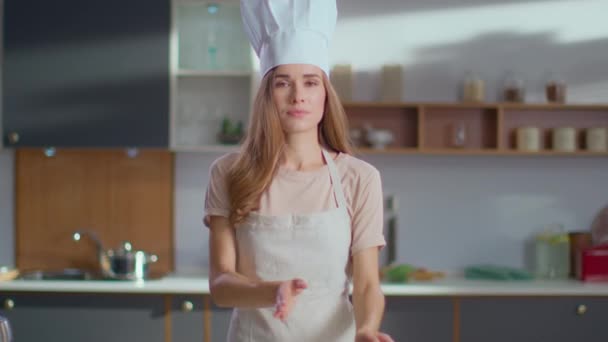 Шеф-повар в варочной шляпе стоит на рабочем месте. Женщина подмигивает в камеру на кухне — стоковое видео