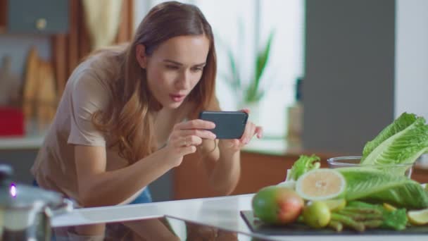 Женщина фотографирует на смартфоне фрукты на кухне. Леди с помощью мобильного телефона — стоковое видео