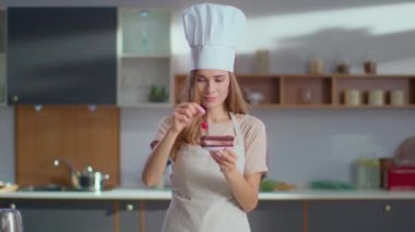 İşyerinde pastayı kirazla süsleyen pastacı. Kameraya bakan kadın.