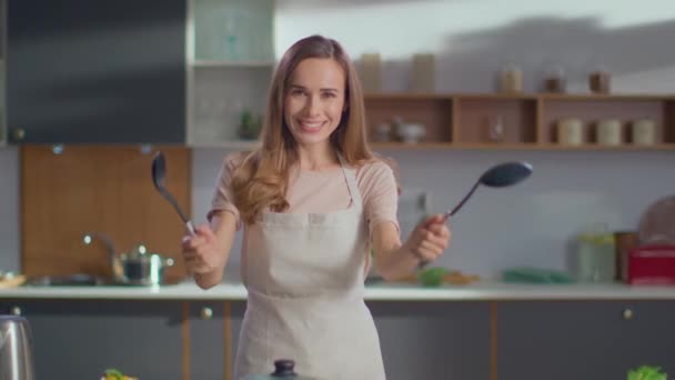 Egy nő kanalakkal a kezében a konyhában. Nő nézi kamera a konyhában — Stock videók