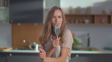 Happy woman dancing on kitchen. Housewife singing song in whisker on kitchen