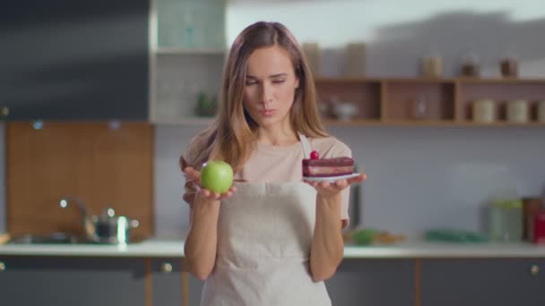 Woman making choice between apple and cake on kitchen. Woman choosing apple — Wideo stockowe