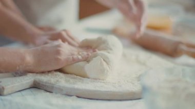 Mother hands helping daughter to knead dough on table at home