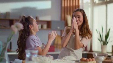 Girl smearing mother nose in flour on kitchen. Family spending time at home