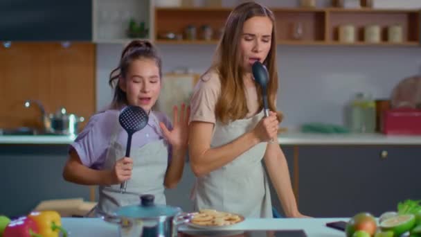 Cheerful mother and daughter singing song in spoons on kitchen — Stock Video