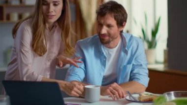 businesswoman and businessman using laptop on domestic kitchen together