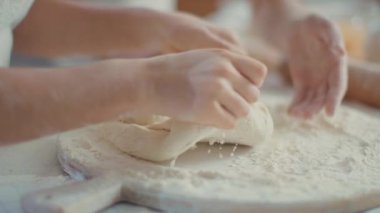 Woman helping daughter to knead dough with flour on kitchen table