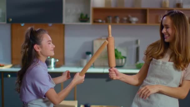 Happy daughter and mother fighting with rolling pins on domestic kitchen — Stockvideo