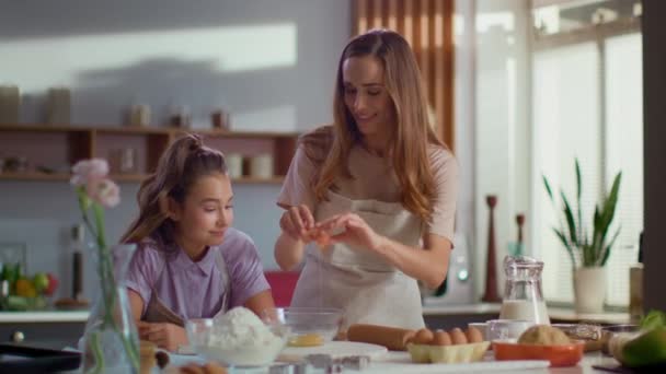 Retrato de la madre y la hija rompiendo huevos en un tazón de vidrio en la cocina — Vídeo de stock