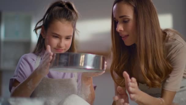 Feliz madre ayudando a su hija a tamizar la harina con tamizador en la cocina — Vídeo de stock