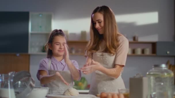 Sorrindo mulher e menina sacudindo farinha na cozinha. Daughner ajudando a mãe . — Vídeo de Stock