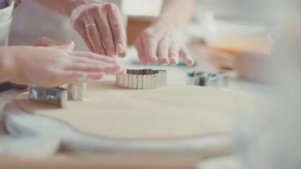 Закройте руки женщине и девушке, разрезая тесто кусачками для печенья на кухонном столе — стоковое видео