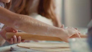 Woman teaching girl to roll dough on kitchen table. Girl hands using rolling pin
