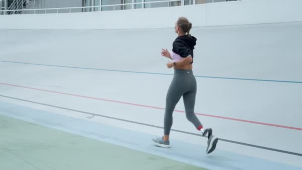 人工肢を持つ女性がトラック上でジョギング。陸上競技場を走る選手 — ストック動画