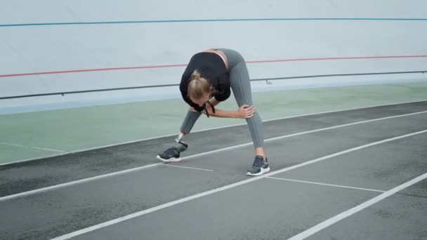 Corredor com perna protética se preparando para o treino na pista. Mulher alongamento corpo — Vídeo de Stock