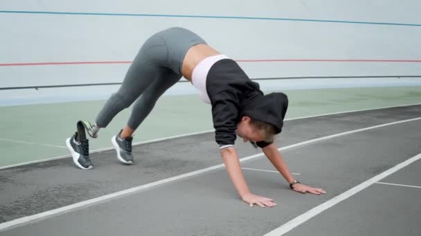 Mujer discapacitada estirando piernas en el estadio. chica practicando yoga en pista deportiva — Vídeos de Stock