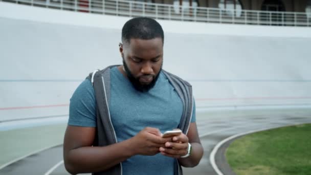 Atleta usando smartphone en el estadio. Sportsman mensaje de texto en el teléfono inteligente — Vídeo de stock