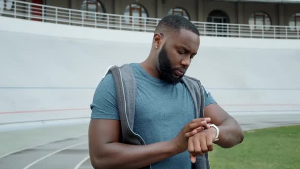 Jogger usando un reloj inteligente en el estadio. Hombre seguimiento de malos resultados después del entrenamiento — Vídeos de Stock