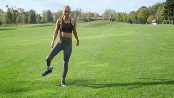 Frau mit Beinprothese wärmt sich im Park. Mädchen beim Sport im Freien — Stockvideo