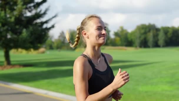 Una deportista sonriente corriendo en el parque verde. Mujer haciendo ejercicio matutino — Vídeos de Stock