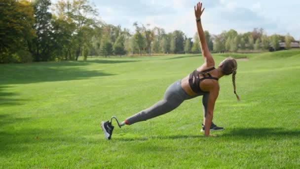 Mozgássérült sportoló nyújtózkodó test a parkban. Lány gyakorló jóga zöld területen — Stock videók