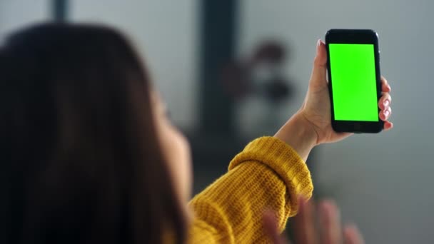 Девушка делает видеозвонок на смартфоне с зеленым экраном. Красивая женщина машет рукой — стоковое видео