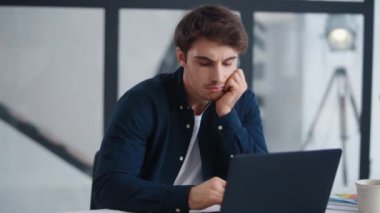 Boring business man looking computer screen in office. Tired guy working laptop