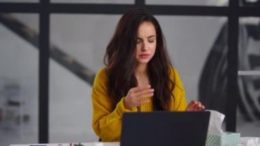 Sick businesswoman getting flu in office. Ill woman sneezing near laptop indoor.