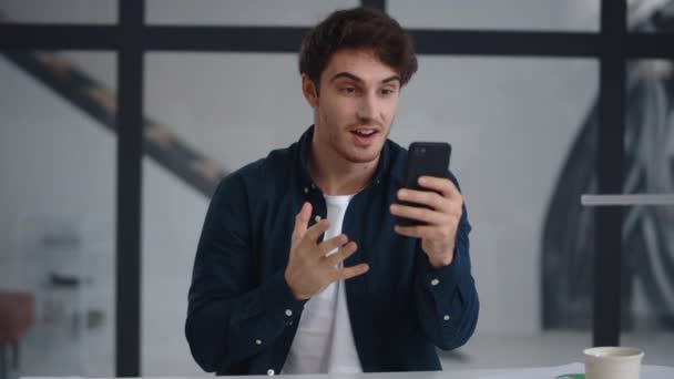 Homme d'affaires souriant faisant appel vidéo sur smartphone dans le bureau . — Video