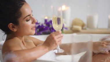Banyo köpüğüyle bacaklarını yıkayan seksi bir kadın. Kız küvette şampanya içiyor.