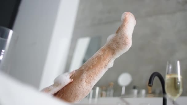 Chiudi piedi donna in bagno di schiuma. Ragazza non riconosciuta lavaggio gambe nella vasca da bagno — Video Stock
