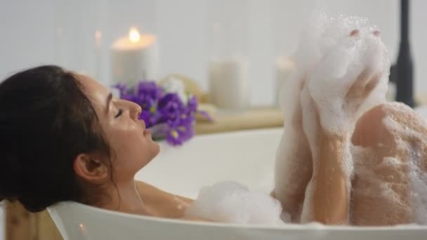 Primer plano mujer sexy jugando con espuma en la bañera. fRelajada chica acostada en el baño — Vídeo de stock