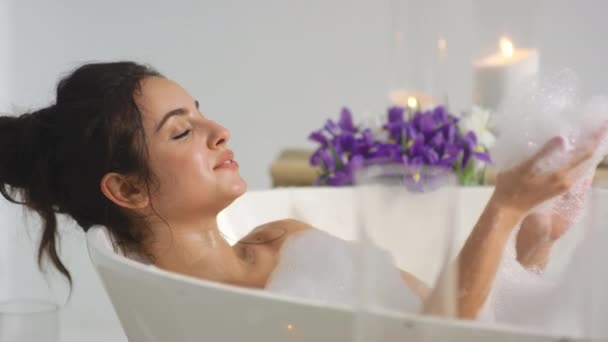 Closeup mulher relaxada soprando espuma no banho. Sorrindo mulher se divertindo com espuma . — Vídeo de Stock