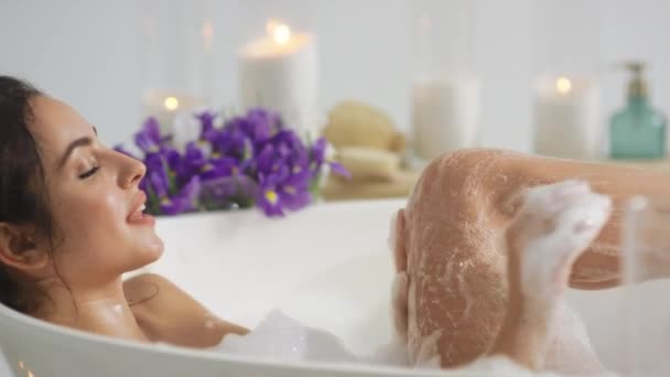 Vista lateral de mujer caliente lavando las piernas con espuma. Chica romántica tomando baño en casa — Vídeos de Stock