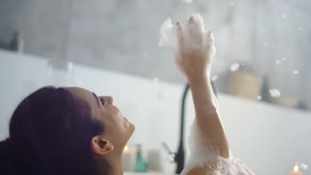 Fechar a mulher relaxada soprando espuma no banheiro. Menina feliz se divertindo com espuma — Vídeo de Stock