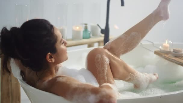 Entspannte Frau mit winkenden Beinen in der Badewanne. Seitenansicht des brünetten Mädchens beim Beinwaschen — Stockvideo