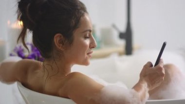 Küvette akıllı telefondan mesaj yazan seksi bir kadın. Cep telefonuyla banyo yapan kız.
