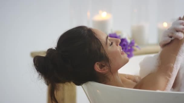 Cilde köpükle dokunan rahat bir kadın. Esmer kadın banyoda dinleniyor. — Stok video