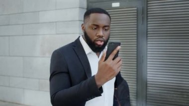 Afro işadamı sokakta kameraya bağırıyor. Müdür dışarıda akıllı telefon kullanıyor.