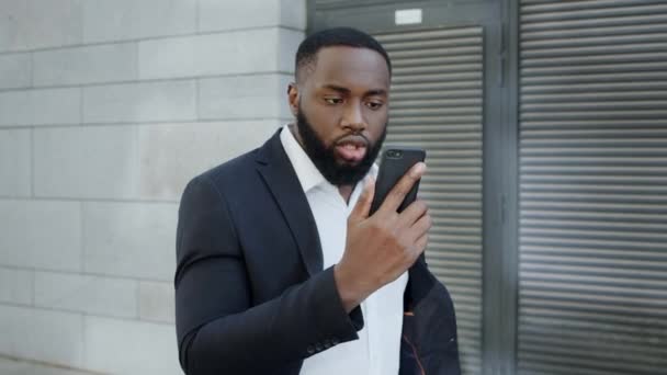 Afro üzletember kiabál a kamera előtt az utcán. A menedzser okostelefont használ a szabadban — Stock videók